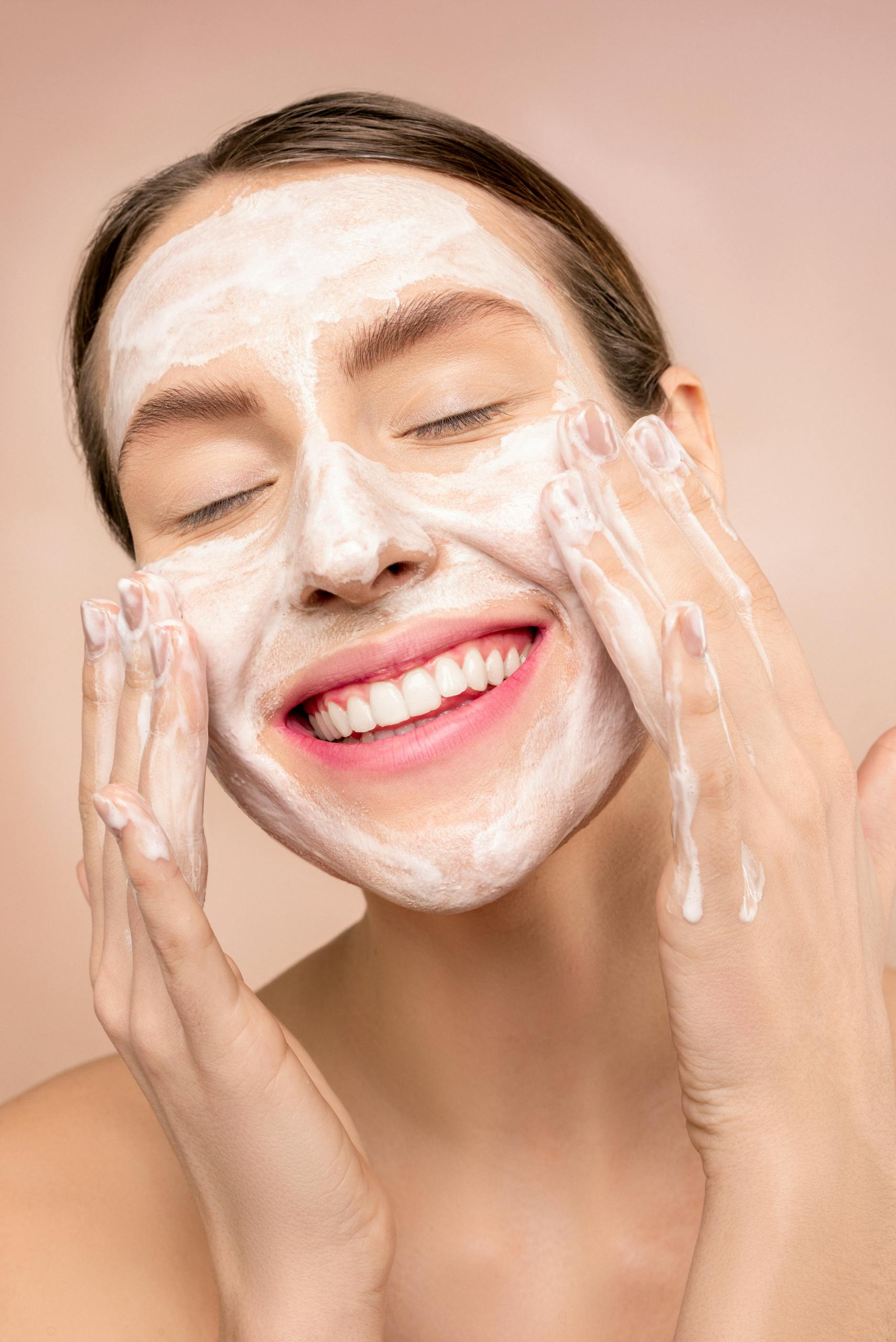 Smiling woman applies facial wash while enjoying her skincare routine, promoting happiness and skin health.