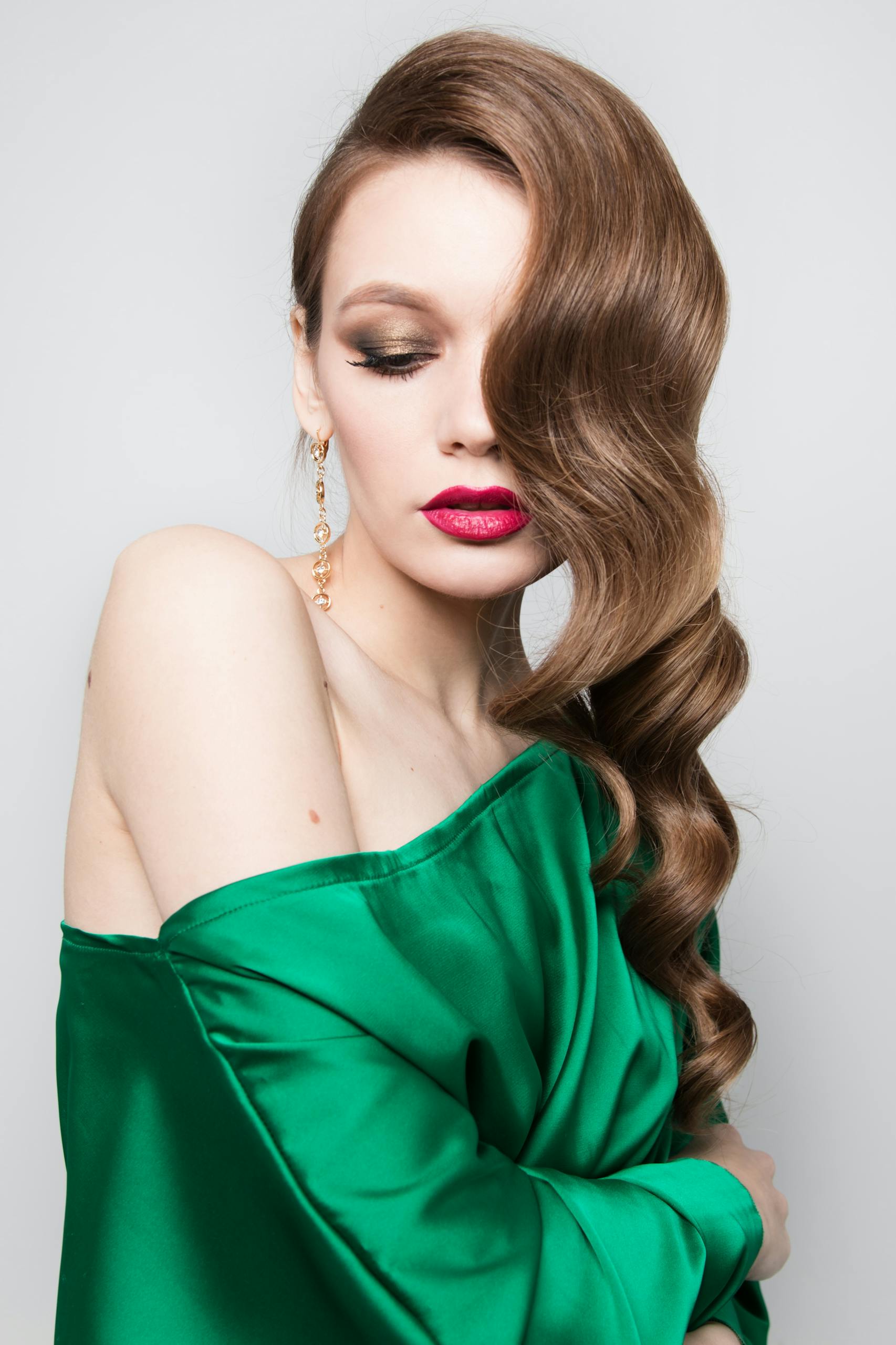 Stylish woman in an off-shoulder green dress, showcasing elegant hair and makeup.